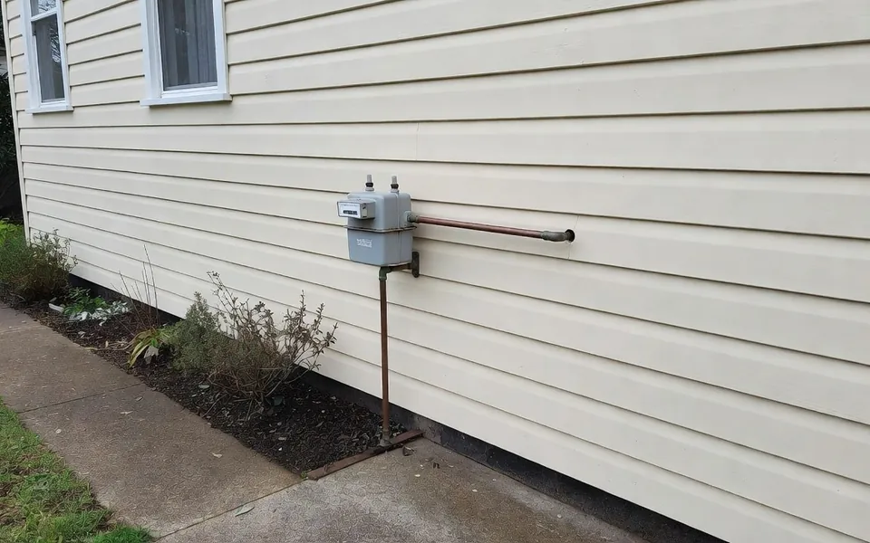 A domestic gas meter on the side wall of a weatherboard house